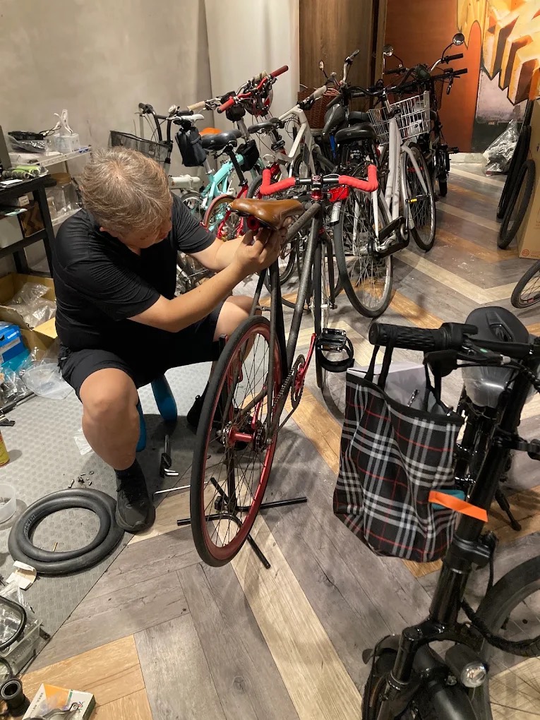 老闆蹲在店內，正在為一台紅色公路車調整座墊